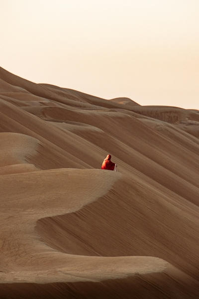 A person in a red cloak on a vast sand dune at golden hour, Ultra