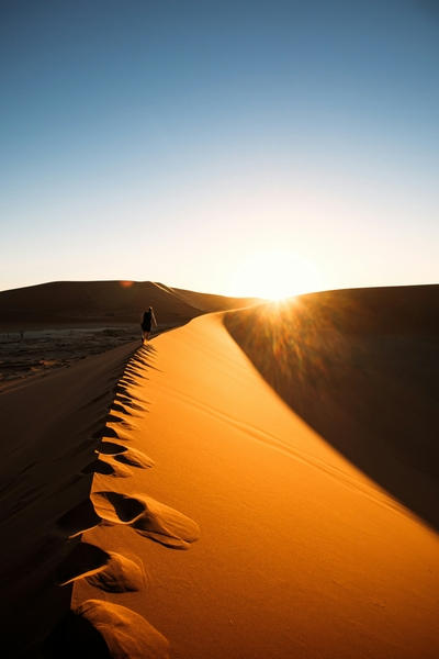 A person walks along a desert sand dune at sunset, Standard