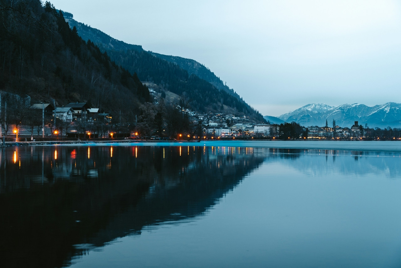 A town with glowing streetlights along a lake reflecting mountains under a cool sky, Standard