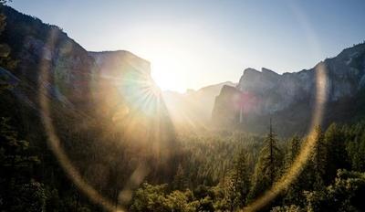 Low sun with lens flare over a forested valley and granite cliffs in Yosemite, Standard